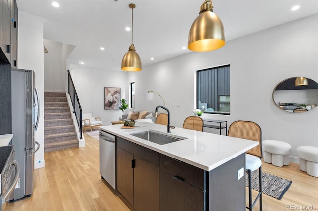 kitchen with a center island with sink, stainless steel appliances, light countertops, open floor plan, and a sink