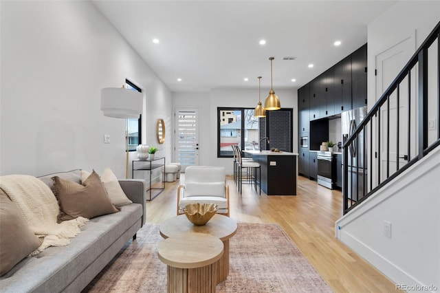 living room featuring stairs, recessed lighting, baseboards, and light wood-style floors