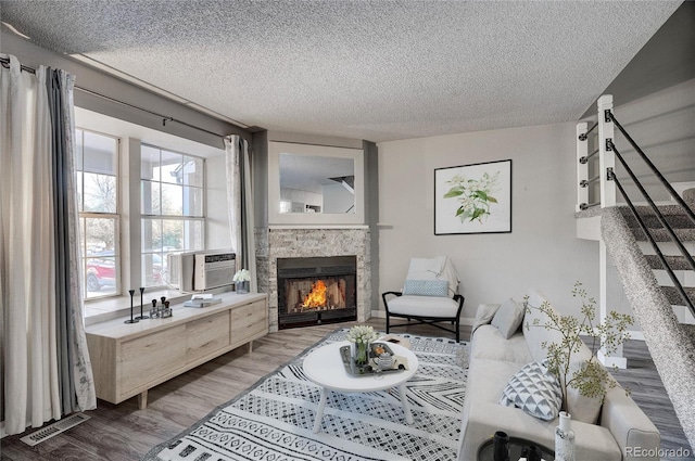 living room featuring a stone fireplace, cooling unit, a textured ceiling, and hardwood / wood-style flooring