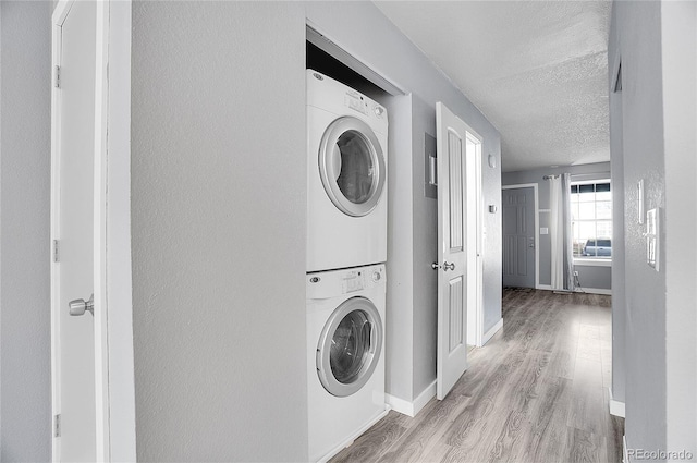 laundry area with light wood-type flooring, a textured ceiling, and stacked washing maching and dryer