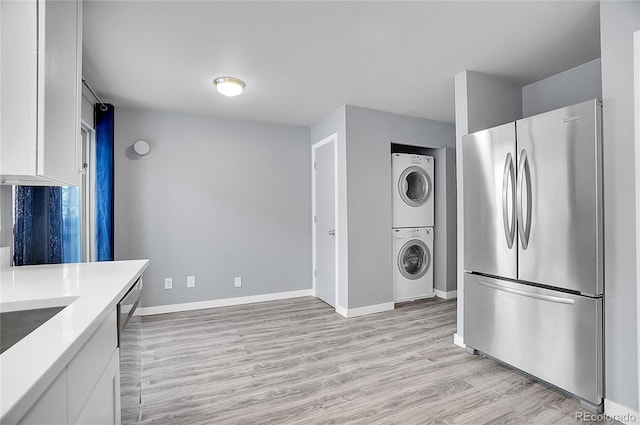 kitchen with white cabinets, light wood-type flooring, stacked washer / dryer, and stainless steel appliances