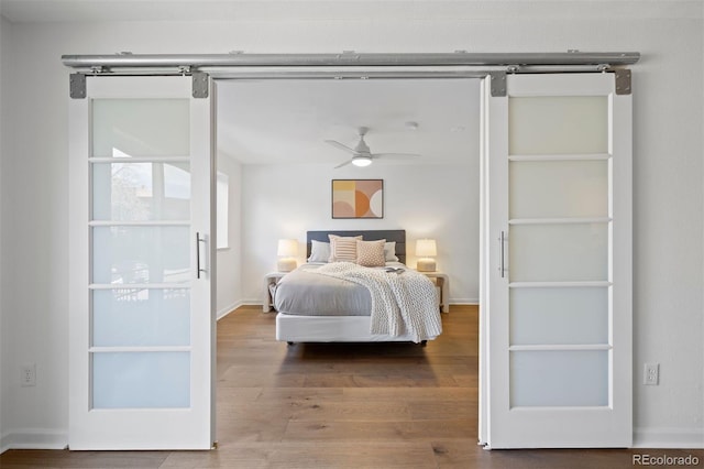 bedroom with a barn door, baseboards, and wood finished floors