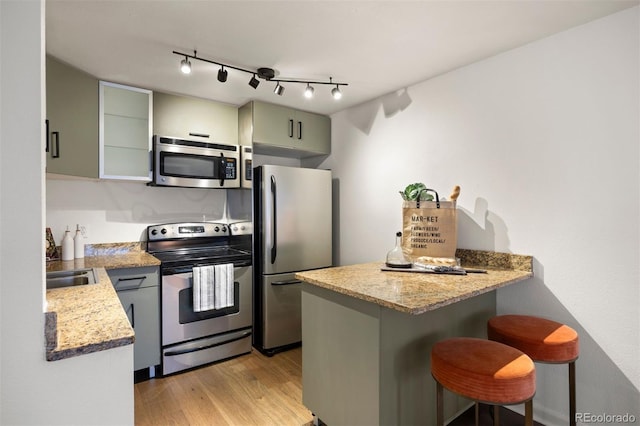 kitchen featuring light wood-type flooring, a kitchen bar, light stone counters, appliances with stainless steel finishes, and a peninsula