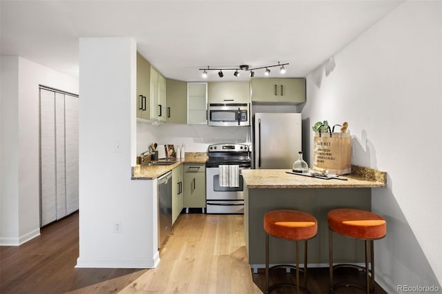 kitchen with a breakfast bar, light wood-style flooring, a peninsula, stainless steel appliances, and green cabinetry