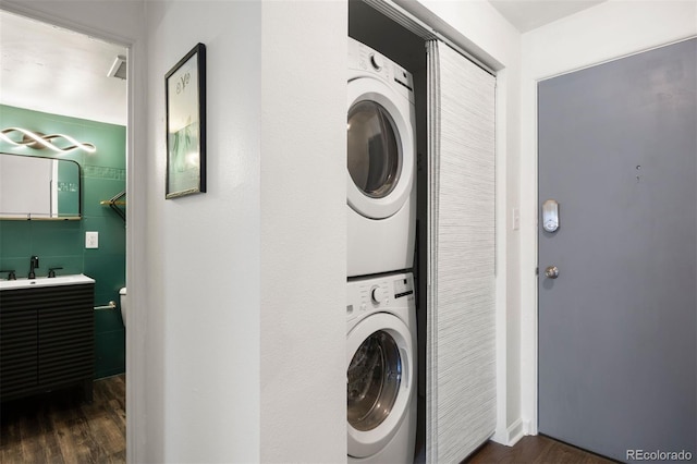 clothes washing area featuring a sink, stacked washer / drying machine, dark wood-style flooring, and laundry area