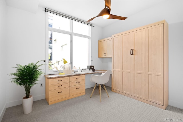 office area featuring built in desk, light colored carpet, and ceiling fan