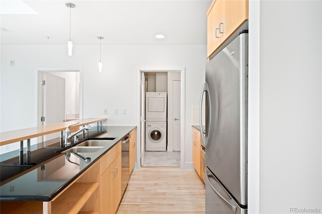 kitchen featuring stainless steel appliances, stacked washer / drying machine, light brown cabinets, and a peninsula