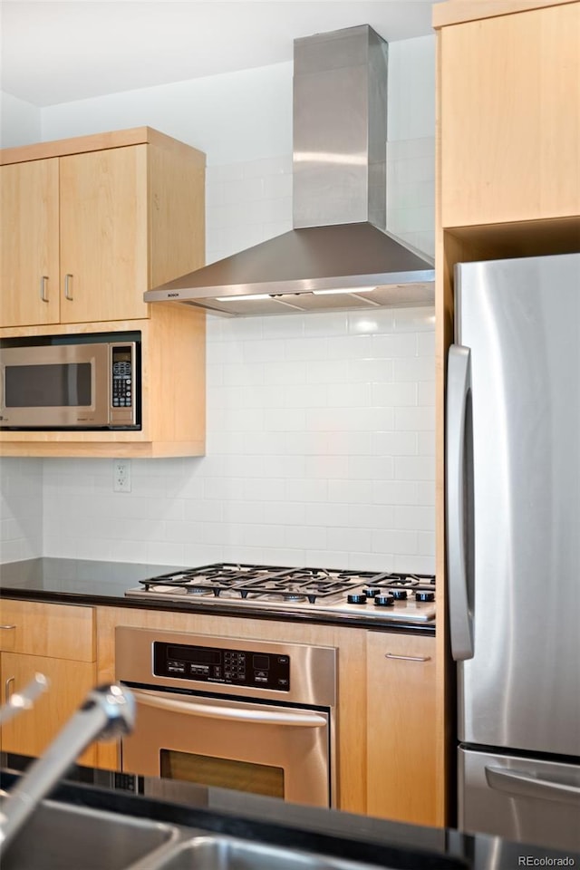 kitchen featuring stainless steel appliances, wall chimney exhaust hood, light brown cabinetry, tasteful backsplash, and dark countertops