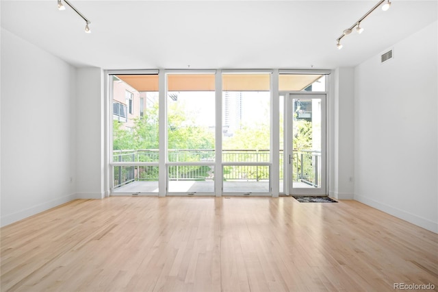 empty room with rail lighting, floor to ceiling windows, healthy amount of natural light, and wood finished floors