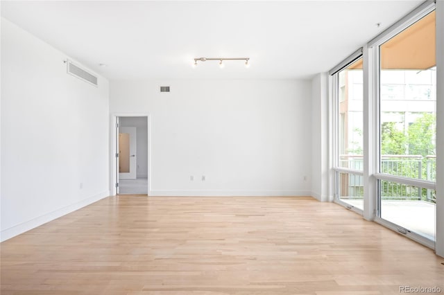 empty room with light wood-style flooring, baseboards, and rail lighting