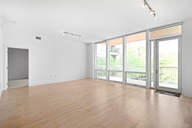 empty room featuring track lighting, light wood-style floors, expansive windows, and baseboards