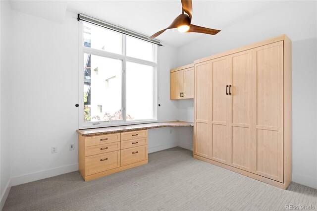unfurnished office featuring built in desk, light colored carpet, ceiling fan, and baseboards