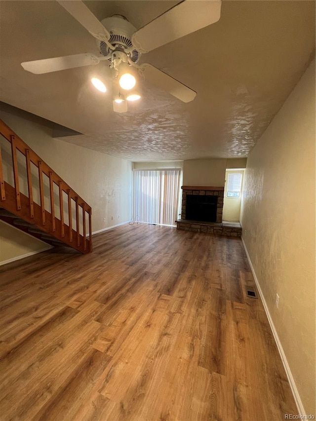 unfurnished living room featuring hardwood / wood-style floors, ceiling fan, a fireplace, and a textured ceiling