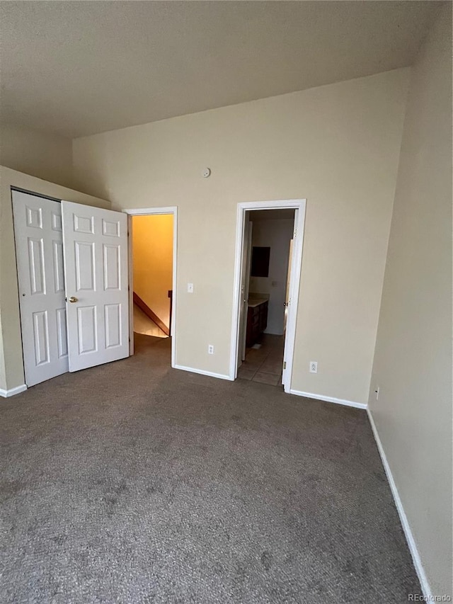 unfurnished bedroom featuring connected bathroom, dark carpet, and a closet