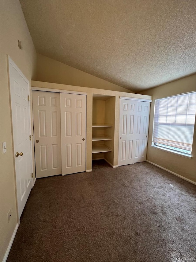 unfurnished bedroom featuring dark carpet, vaulted ceiling, a textured ceiling, and two closets