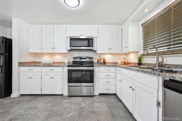 kitchen featuring appliances with stainless steel finishes, a sink, white cabinets, and stone counters