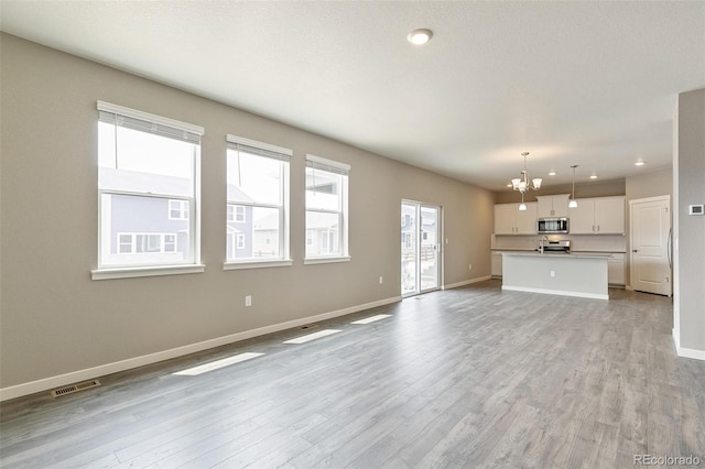 unfurnished living room featuring a notable chandelier, light hardwood / wood-style floors, and a textured ceiling