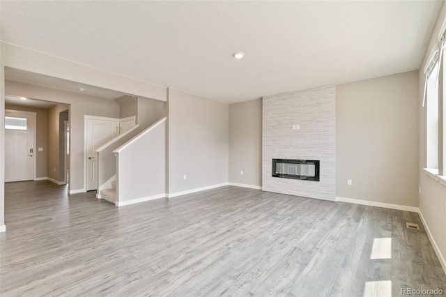 unfurnished living room with a large fireplace, heating unit, and light hardwood / wood-style flooring