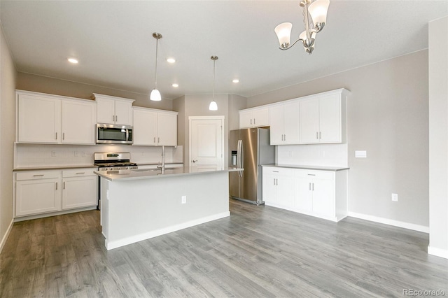 kitchen featuring hanging light fixtures, appliances with stainless steel finishes, a center island with sink, and white cabinets