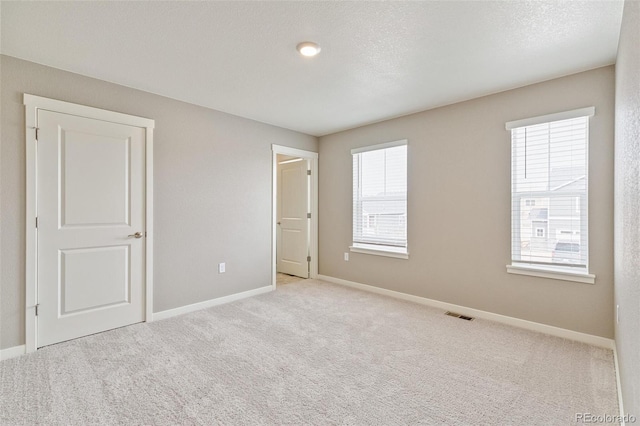 unfurnished room featuring a textured ceiling, light colored carpet, and a healthy amount of sunlight