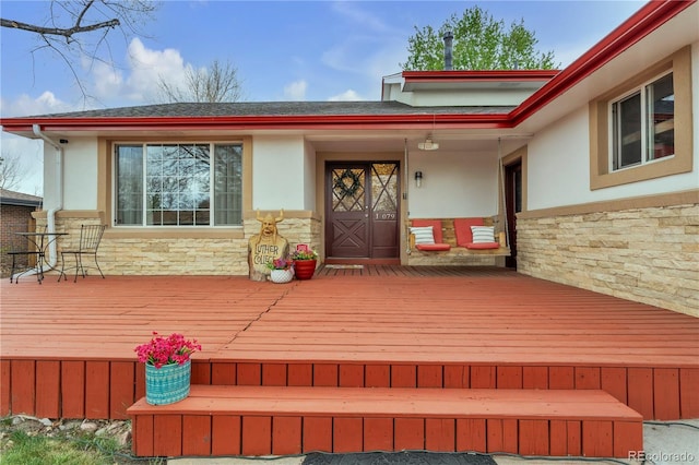 doorway to property with a wooden deck, stone siding, and stucco siding