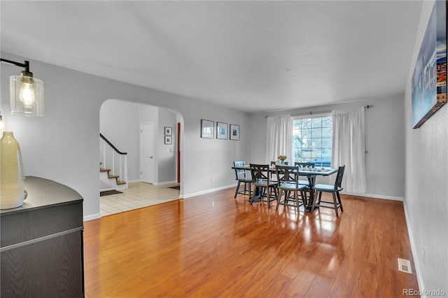 dining area with visible vents, wood finished floors, baseboards, stairway, and arched walkways