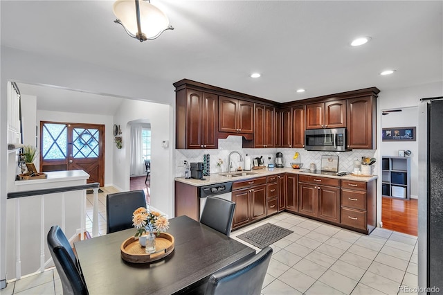 kitchen with arched walkways, tasteful backsplash, a sink, light countertops, and stainless steel appliances