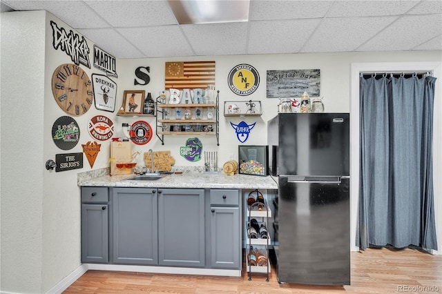 bar with bar, a paneled ceiling, a sink, freestanding refrigerator, and light wood-style floors