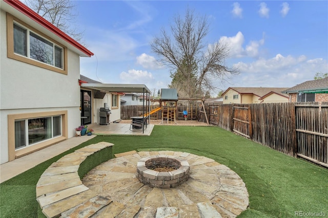 view of yard featuring a fenced backyard, a patio, a playground, and a fire pit