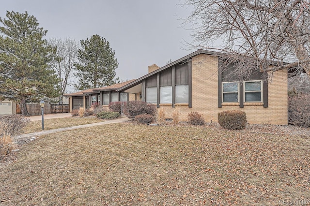 view of front of house featuring an attached garage, brick siding, concrete driveway, a chimney, and a front yard