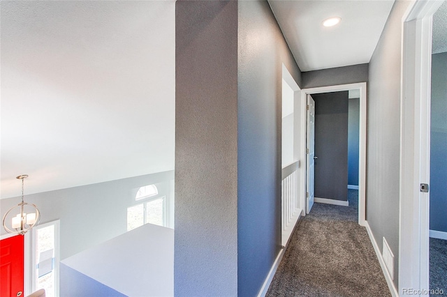 hall with an inviting chandelier and dark colored carpet