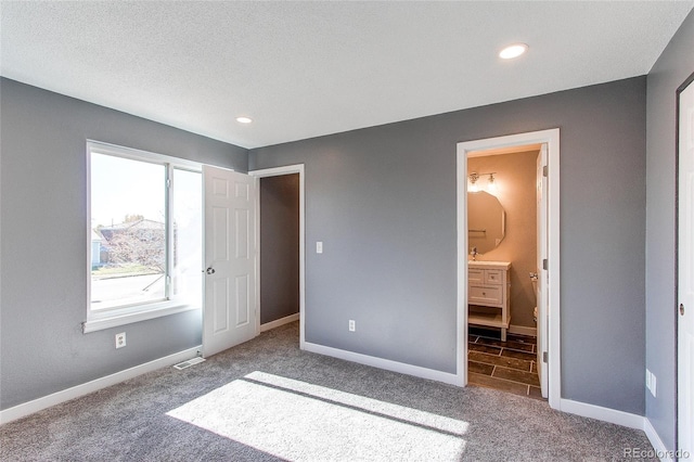 unfurnished bedroom with a textured ceiling, carpet flooring, and ensuite bath