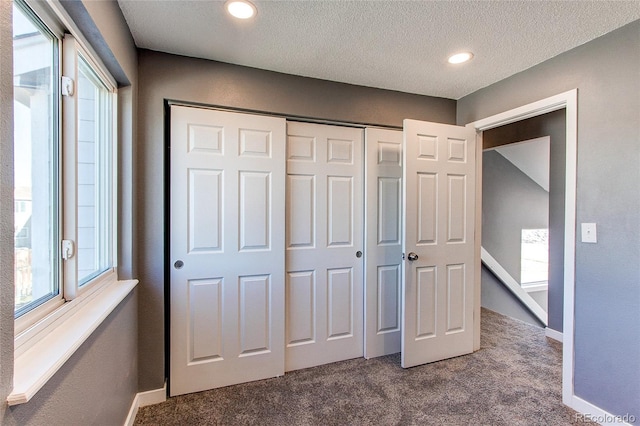 unfurnished bedroom with multiple windows, a closet, carpet flooring, and a textured ceiling