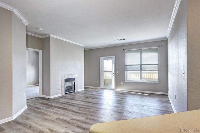 unfurnished living room featuring light hardwood / wood-style flooring, ornamental molding, and a tiled fireplace