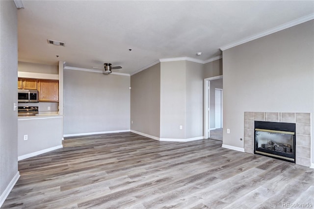 unfurnished living room featuring ceiling fan, ornamental molding, a tile fireplace, and light hardwood / wood-style flooring