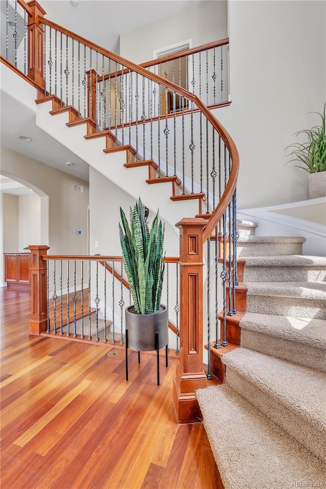 stairway featuring arched walkways, wood finished floors, and a towering ceiling
