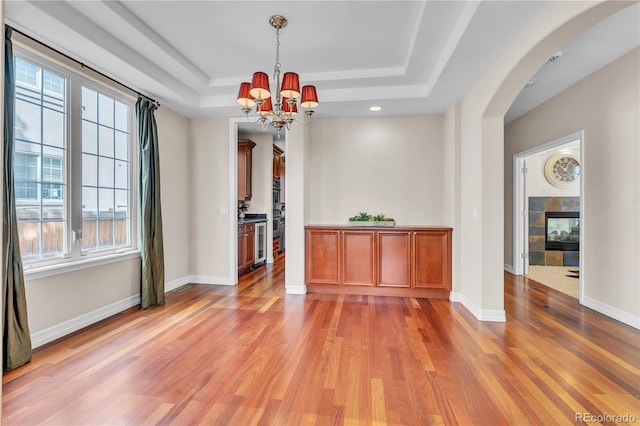 interior space featuring arched walkways, a tray ceiling, plenty of natural light, and light wood finished floors