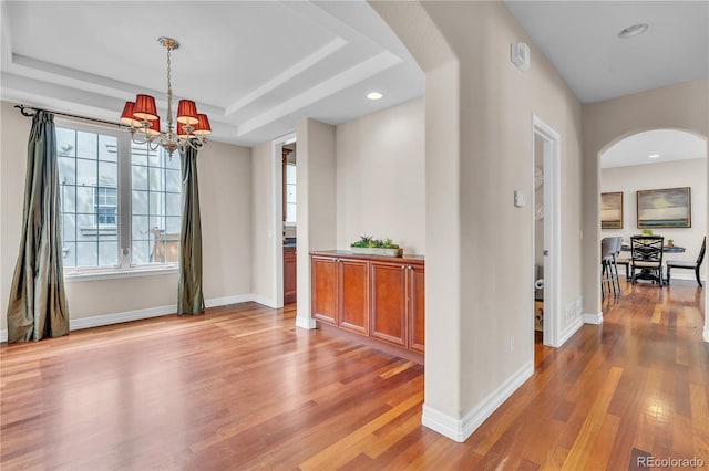 interior space featuring light wood-type flooring, arched walkways, baseboards, and an inviting chandelier