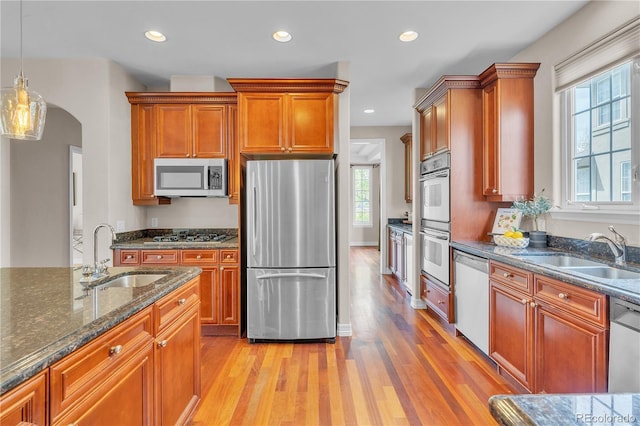 kitchen featuring dark stone counters, appliances with stainless steel finishes, a sink, and light wood-type flooring