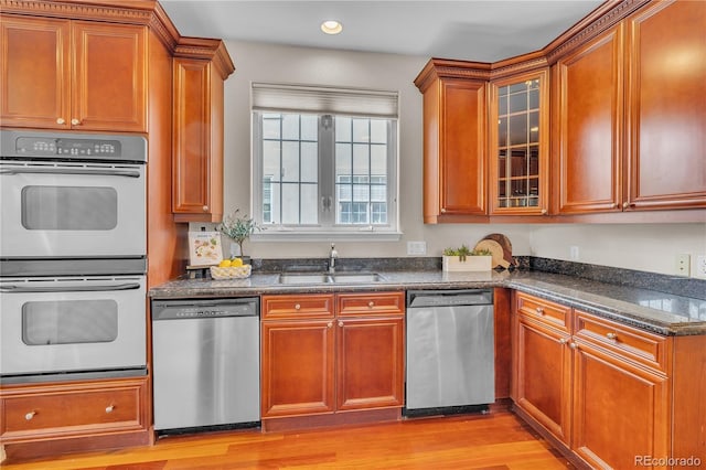 kitchen featuring glass insert cabinets, light wood-style floors, a sink, dark stone countertops, and appliances with stainless steel finishes