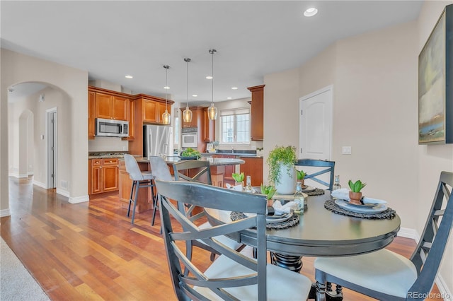 dining space with light wood-style floors, arched walkways, baseboards, and recessed lighting