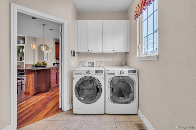 clothes washing area featuring cabinet space, baseboards, light tile patterned floors, visible vents, and washer and clothes dryer