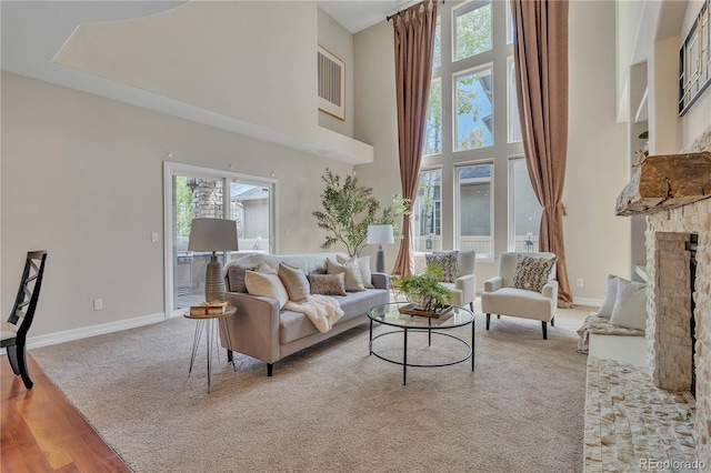 living area with a stone fireplace, baseboards, light wood finished floors, a high ceiling, and light carpet