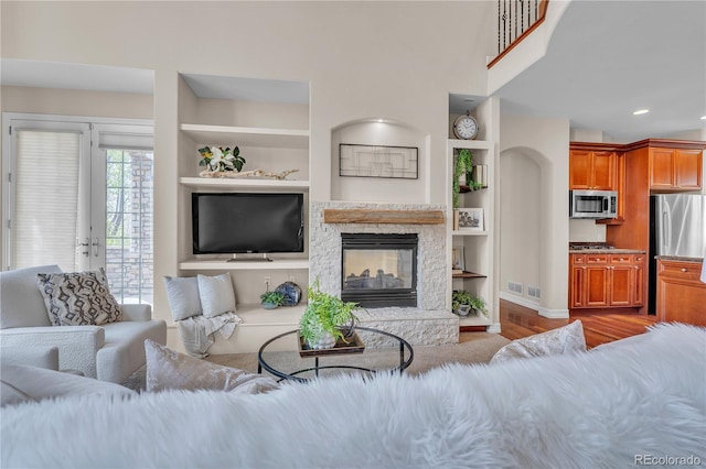 living room with a stone fireplace, built in features, wood finished floors, baseboards, and recessed lighting