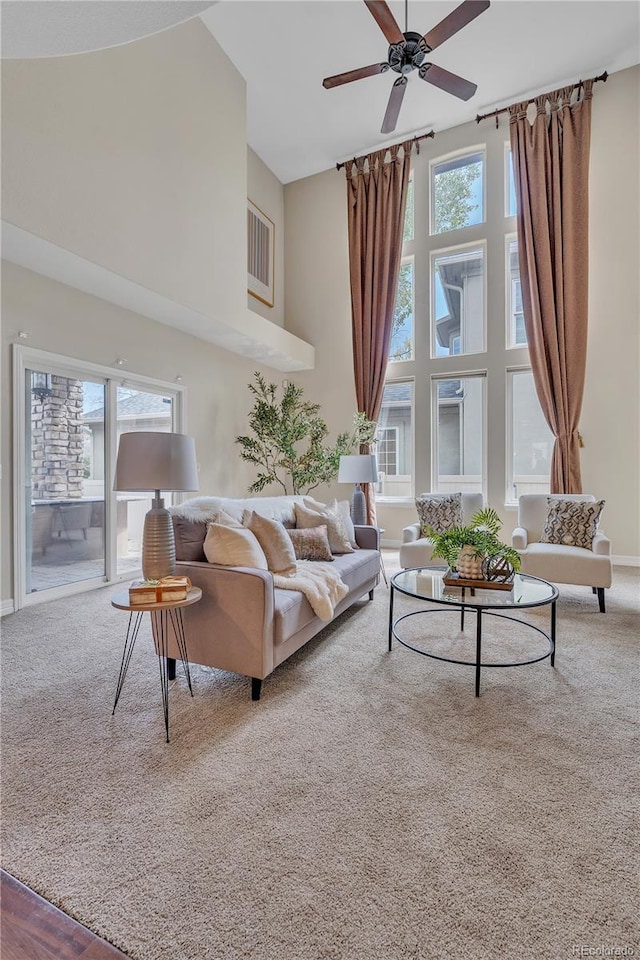 living room featuring carpet floors, a ceiling fan, baseboards, and a towering ceiling