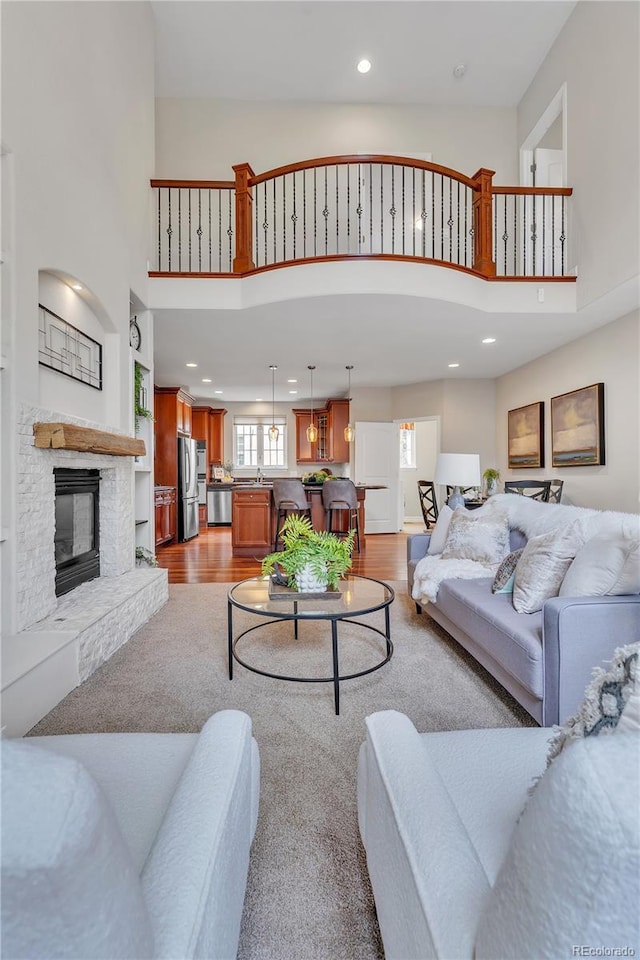 living area featuring light wood-style floors, recessed lighting, a high ceiling, and a stone fireplace