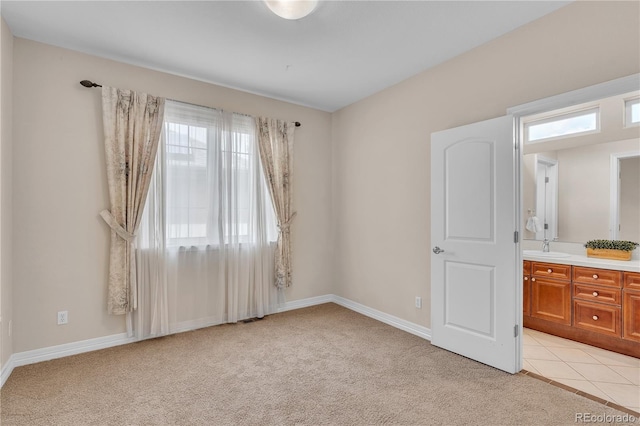 unfurnished bedroom with connected bathroom, light tile patterned flooring, light colored carpet, a sink, and baseboards