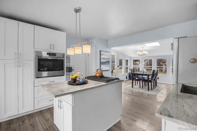 kitchen featuring wood finished floors, light stone countertops, an inviting chandelier, stainless steel appliances, and white cabinetry