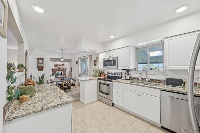 kitchen with recessed lighting, a peninsula, white cabinets, appliances with stainless steel finishes, and a sink