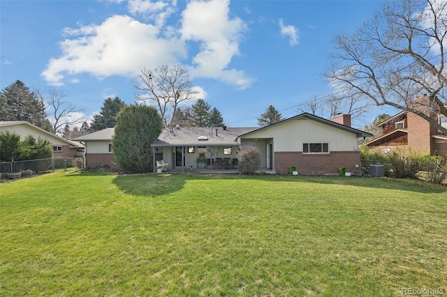 back of house with a chimney, a lawn, fence, and brick siding